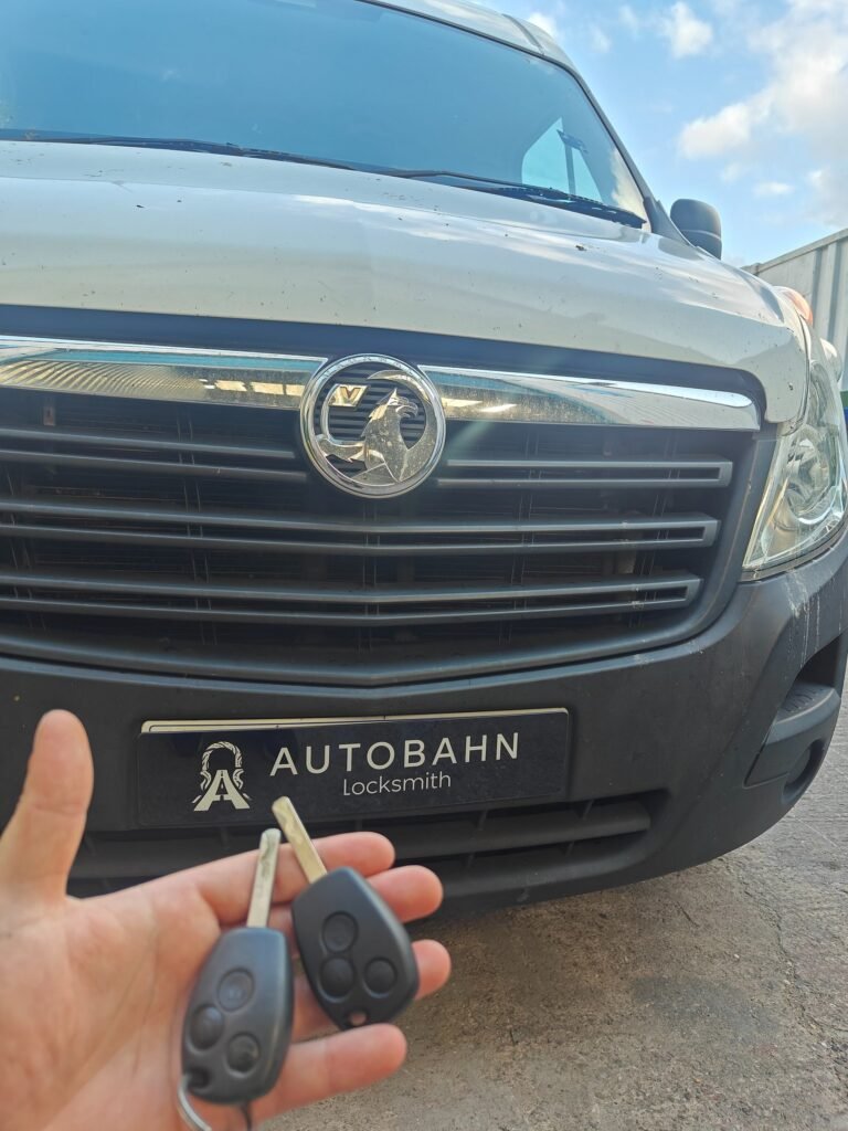 Two remote car keys held up in front of an Autobahn Locksmith van