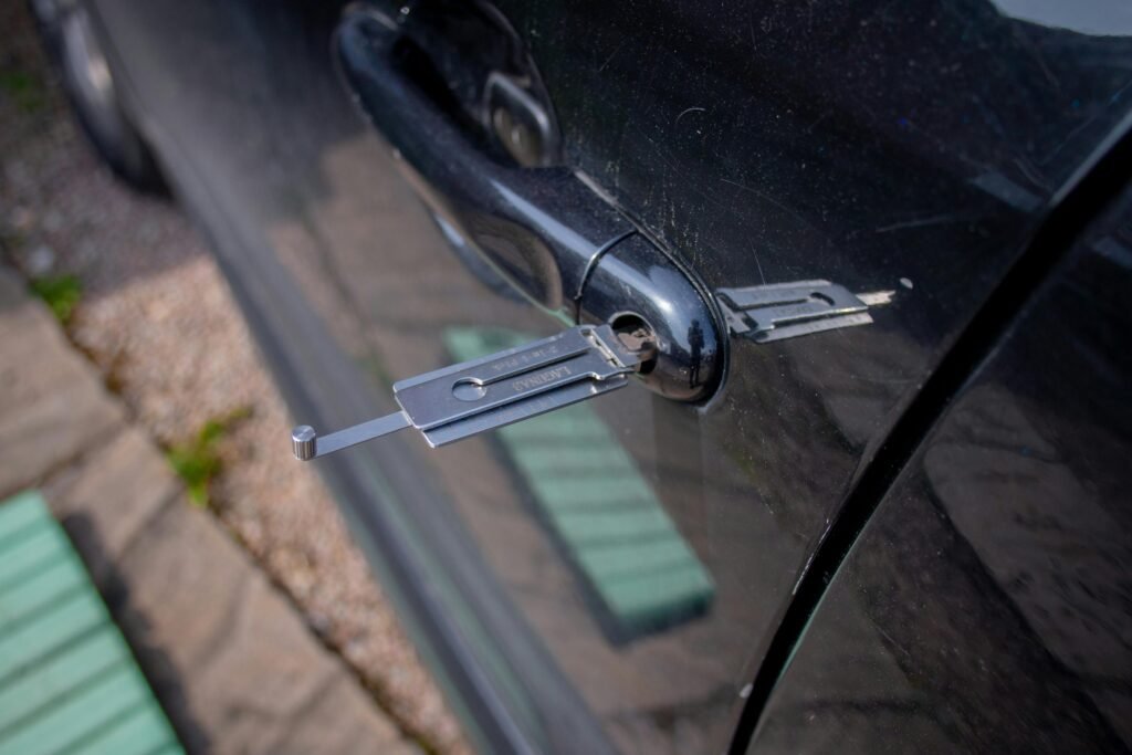 An auto locksmith's decoder tool inserted into the door lock of a black car